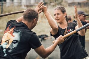 Dva lidé cvičí techniky s tyčemi při venkovním tréninku Kali